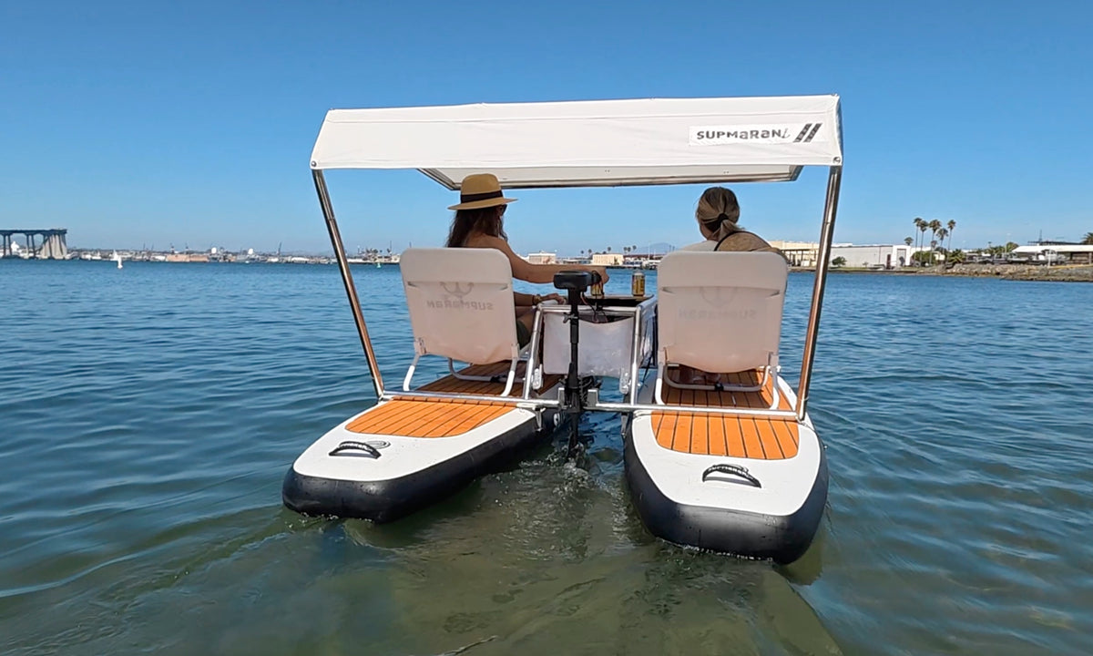 Two women cruising away on a motorized Supmaran catamaran, sitting comfortably under the canopy.