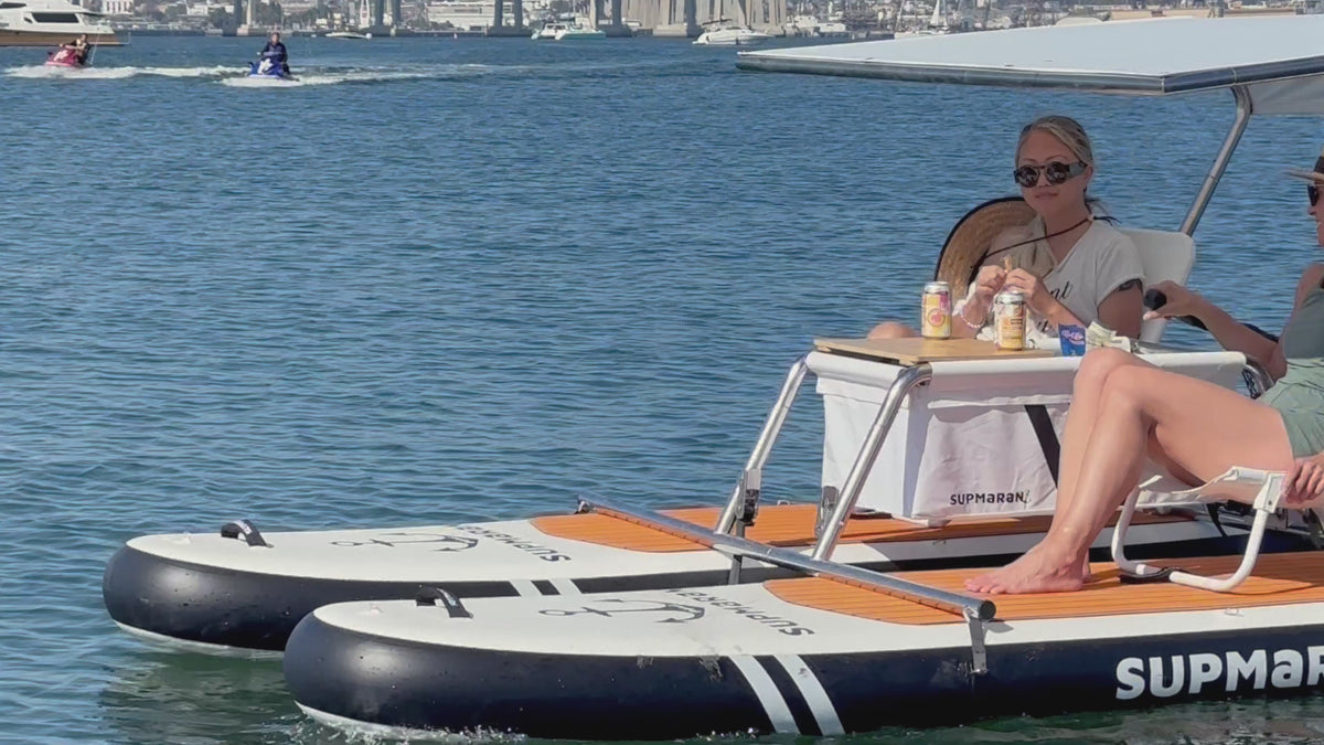 Friends easily carrying the lightweight Supmaran catamaran to the water and relaxing on the deck under a sunshade while cruising with an electric motor.